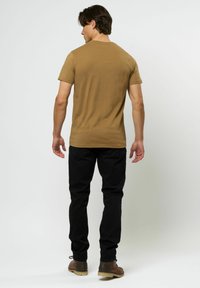 Tricou din bumbac khaki cu gât rotund, cu mâneci scurte și o textură netedă, asortat cu pantaloni negri și pantofi maro.