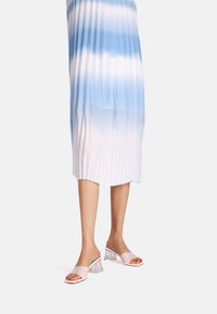 Abito plissettato in gradiente di blu, che passa al bianco. Mules con tacco trasparente, dalla superficie lucida e con punta aperta, completano l'outfit.