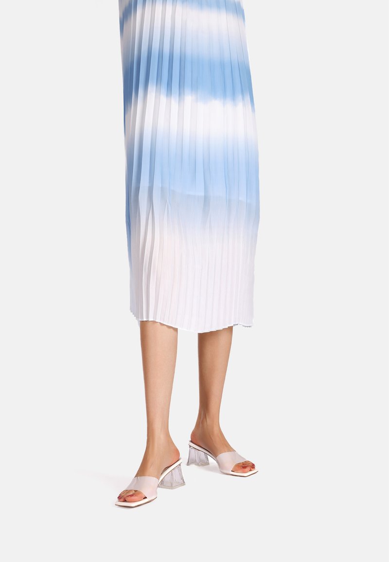 Abito plissettato in gradiente di blu, che passa al bianco. Mules con tacco trasparente, dalla superficie lucida e con punta aperta, completano l'outfit.