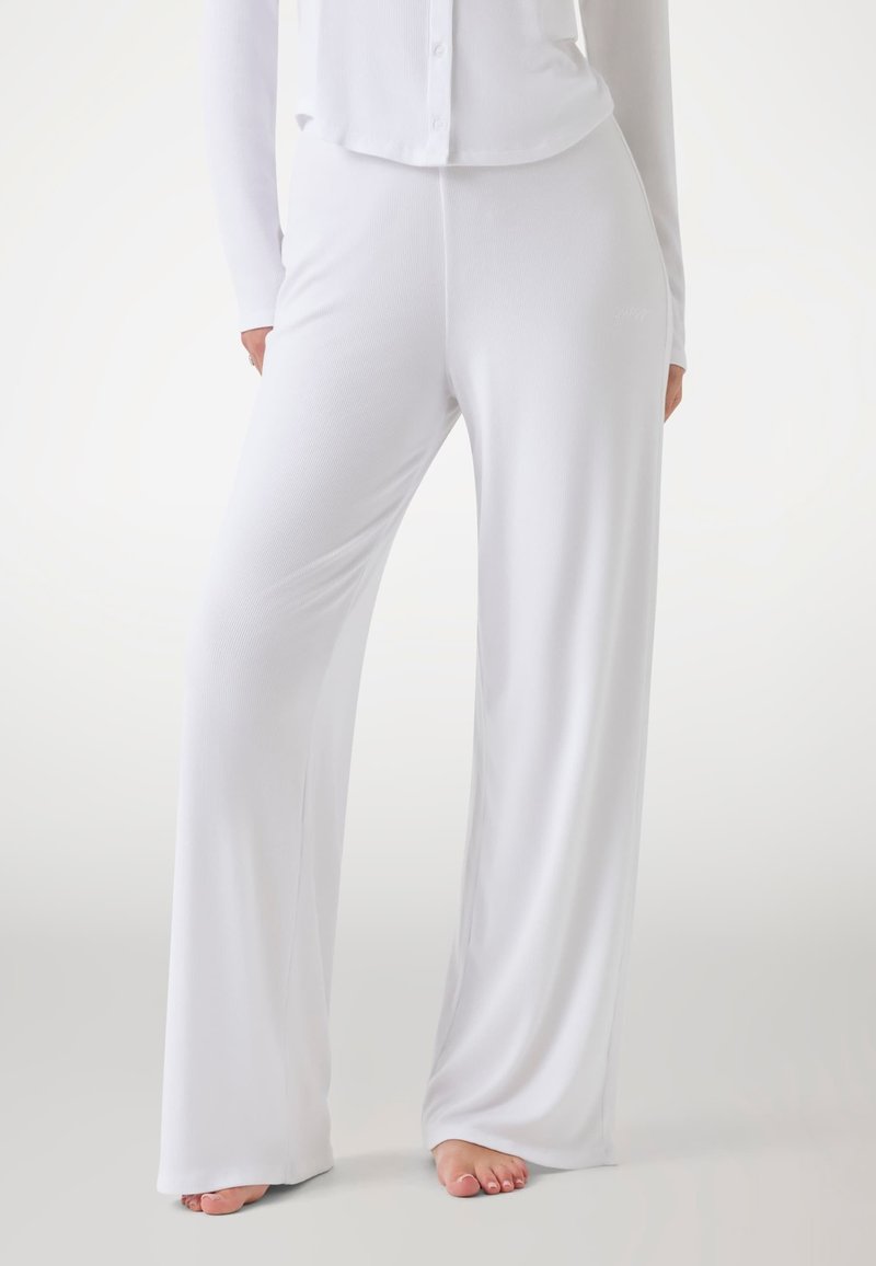 White, ribbed wide-leg pants made of soft fabric, featuring a relaxed fit and a smooth texture. Accentuated with minimal detailing.