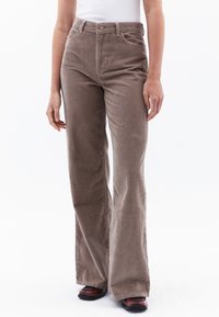 Bruine fluwelen broek met uitlopende pijpen en een geribbelde textuur, met een hoge taille, voorzakken en details met zilverkleurige knopen.