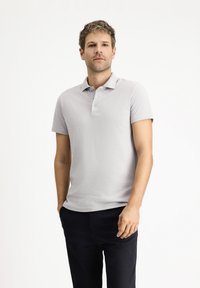Graues Poloshirt aus strukturiertem Stoff, mit drei Knöpfen am Kragen und kurzen Ärmeln, kombiniert mit dunkler Hose.