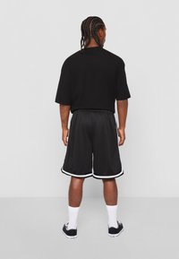 T-shirt noir oversize associé à un short de sport noir avec des rayures blanches sur les côtés. Porté avec des chaussettes blanches et des baskets noires.