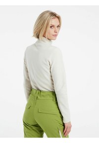 Maglione a collo alto in pile di colore beige chiaro, presenta una superficie testurizzata. Abbinato a pantaloni verde alto in vita con tasche e zip.