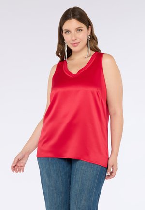 Top senza maniche in raso rosso con scollatura a V, forma fluida e texture liscia. Indossato con pantaloni a vita alta blu con righe verticali.