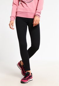 Leggings elásticos negros con un ajuste ceñido, combinados con un sudadera rosa y zapatillas deportivas negras con acentos rosas y una suela texturizada.
