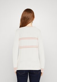 Haut à manches longues blanc avec deux bandes pastel roses horizontales dans le dos et des accents assortis sur les manches. Texture douce.