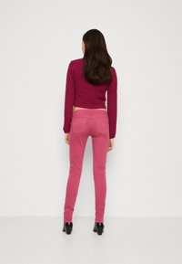 Pantalones de mezclilla rosa con un ajuste slim y bolsillos traseros, combinados con un suéter de punto burdeos corto. Textura suave, sin patrones visibles.