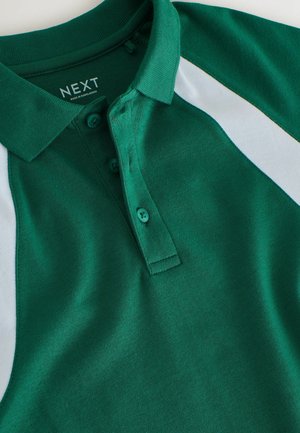 Zöld galléros póló puha anyagból, háromgombos plakkal és fehér oldalsó panel díszítéssel. A címke "NEXT" felirattal és ápolási információkkal.