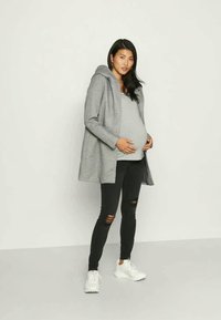 Sivý kapucňový kabát na sivom topu, skombinovaný s čiernymi roztrhnutými džínami a bielymi teniskami. Model je stredobodom pozornosti, s viditeľným zaobleným bruchom.