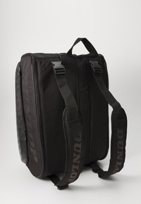 Schwarze Sporttasche aus langlebigem Material mit zwei Schulterriemen. Verfügt über Reißverschlüsse und "Dunlop"-Markenlogo auf einer Seite. Rechteckige Form.