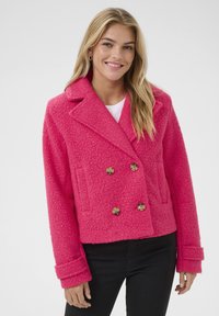 Veste double boutonnage rose vif en tissu texturé, grandes revers, deux poches avant et boutons dorés. Longueur courte et manches larges.