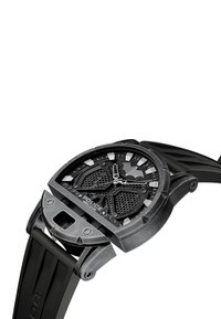 Črn časovnik s teksturiranim ohišjem, metuljčast motiv na številčnici in oglatimi kazalci. Ima gumijast trak in zapletene mrežaste detajle.