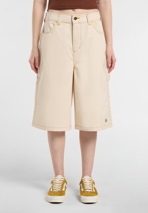 Beige cargo shorts with visible stitching, two side pockets, and a straight cut. Paired with yellow suede sneakers.