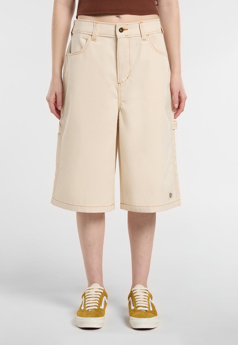 Pantaloni cargo beige con cuciture visibili, due tasche laterali e taglio dritto. Abbinati a sneaker in suede gialle.