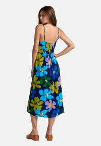 Bunt gemustertes Maxikleid mit Spaghettiträgern, gerafftem Oberteil und einem marineblauen Hintergrund, der mit großen blauen, grünen und lila Blumen verziert ist.