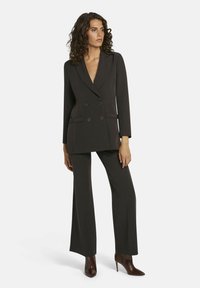 Zwarte dubbelgeknoopte blazer met notch-lapels, zijzakken en bijpassende zwarte wijde broek. Model draagt bruine puntige hakken.