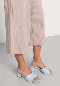 Light blue block-heeled mules with an open toe and smooth patent finish, paired with pale ribbed wide-leg trousers.