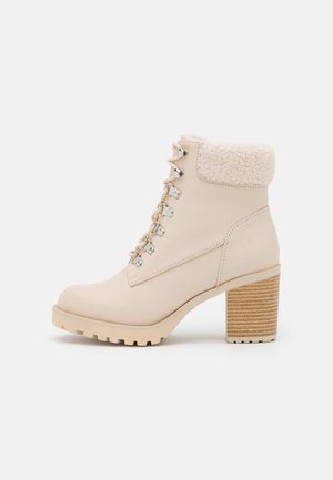 Beige leren enkelboot met een gestructureerde crèmekleurige nepbont kraag, voorzien van metalen oogjes en een stevige, geprofileerde houten hak.