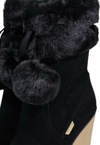 Černé semišové kotníkové boty s měkkým syntetickým kožíškem, zdobené dvěma bambulkami a zlatou visačkou. Mají špičatou špičku a štosovanou patu.