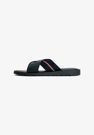Zwarte teenslippers met kruisbanden van textuurrubber en elastiek, voorzien van een rood-witte streepaccent. Platte, geribbelde zool voor grip.