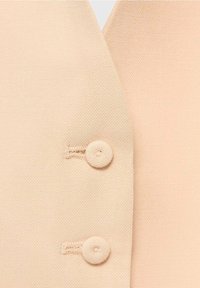 Pfirsichfarbener Blazerstoff mit strukturierter Oberfläche, der zwei passende runde Knöpfe vorne und einen V-förmigen Ausschnitt aufweist.