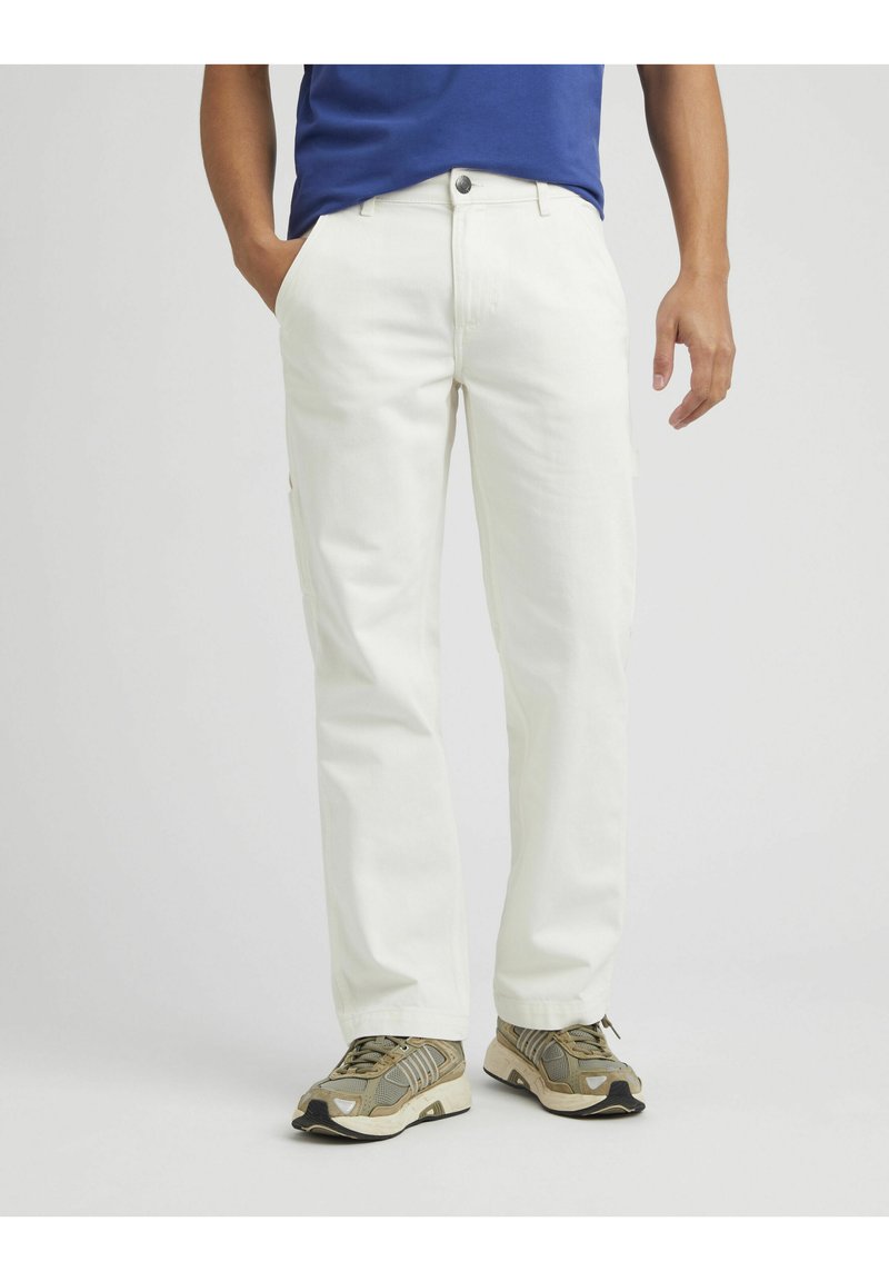Pantalon en coton blanc avec une coupe droite, comportant des poches avant et des poches cargo sur le côté. Associe à des baskets grises et beiges.