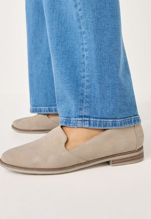Light grey suede loafers with a cut-out design, featuring a flat sole with subtle horizontal stripes, paired with blue denim jeans.