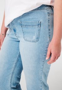 Jeans en denim bleu clair avec une coupe slim, dotés d'une poche arrière et d'un léger effet délavé. Le tissu a une texture lisse et une couture standard.