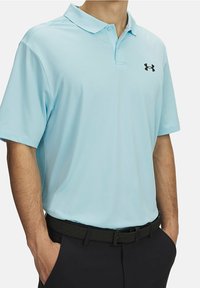 Camisa polo de color azul claro hecha de una tela suave, con cuello y mangas cortas; presenta un logotipo negro de Under Armour en el pecho.