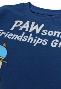 T-shirt en coton bleu avec texte brodé blanc "PAWsome Friendships" et un personnage de dessin animé portant une casquette bleue.
