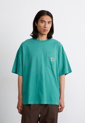 Turquoise oversized cotton t-shirt with short sleeves, a chest pocket, and a small square logo patch in the upper left corner.