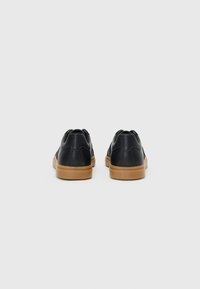 Black leather sneakers with a textured finish, gum rubber soles, and subtle stitching details at the heel. Rear view showing both shoes.