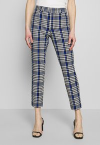 Pantaloni a scacchi che presentano una combinazione di colori nero, bianco e blu. Lunghezza cropped, vestibilità sartoriale, e la trama del tessuto è liscia e strutturata.