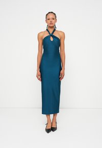 Turkizna, telesna halterneck obleka s detajlom v obliki ključavnice, mehka tkanina in dolžina do sredine meč. Nosi se z črnimi salonarji s koničastim nosom.