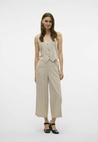 Mono de rayas verticales beige con escote en V, cierre de botones y diseño de pierna ancha; combinado con zapatos negros de tacón cuadrado.