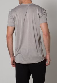 Grå kortärmad t-shirt med rund halsringning, tillverkad av ett mjukt, lätt material. Bakifrån visar den en figurnära passform och minimala sömmar.