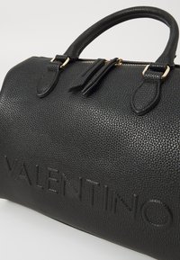 Juoda odinė rankinė su akmenuota tekstūra, auksinė užtrauktukas, dvigubi viršutiniai rankenėlės ir iškilmingas "VALENTINO" logotipas šone.