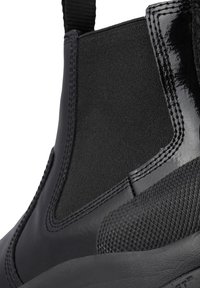 Botines negros con paneles laterales elásticos, suela de goma texturizada, acabado de cuero suave y talón reforzado para mayor durabilidad.