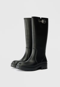 Bottes en caoutchouc noires mi-mollet avec une texture lisse, un large talon et un détail de boucle sur le côté. Comprend des coutures renforcées et une semelle robuste.