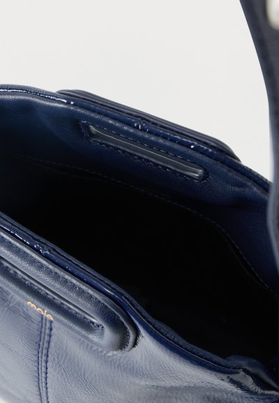 Τσάντα χειρός από δέρμα σε σκούρο μπλε ναυτικό χρώμα με ανοιχτό επάνω μέρος που δείχνει το σκούρο κενό εσωτερικό και ραμμένες άκρες, αναδεικνύοντας υφή και λεπτομέρειες του χερούλιου.