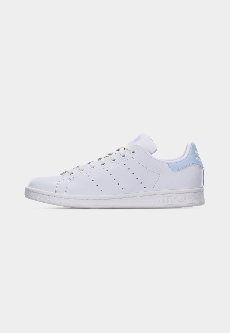 Hvid lavtop sneaker med lyseblåt hælflig, perforerede sidestreger, hvide snørebånd og flad sål på ensfarvet baggrund.