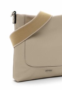 Beige Leder-Crossbody-Tasche mit breitem, hellbraunem Stoffriemen und silbernem Metalllogo "SURI FREY" auf der Vorderseite.