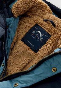 Jasje met marineblauwe buitenkant en zachte bruin fleece voering, met een "NEXT" merklabel waarop een ontwerp van bergen en bomen staat.