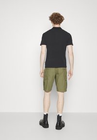 Polo shirt nero a maniche corte abbinato a pantaloni cargo verdi oliva, dotati di tasche laterali e un fit rilassato. Stivali in pelle nera completano l'outfit.