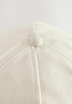 Cască albă cu țesătură texturată, având un vârf rotund și un buton central. Cusăturile vizibile și o suprafață netedă.