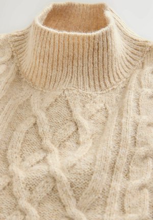 Krämfärgad kabelstickad tröja med hög ribbad krage, med texturerade mönster genom hela plagget och en mjuk, fluffig finish.