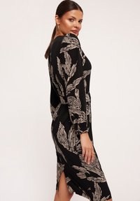 Czarna sukienka z wzorem liści w beżowym kolorze. Posiada długie rękawy, dopasowany fason, boczne rozcięcia i gładką fakturę. Dekoracyjne detale na rękawach.