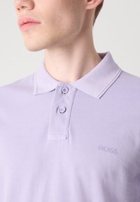 Lyse lilla polo skjorte med teksturert stoff, klassisk krage, to-knaps placket og et tonalt "BOSS" logo på brystet.