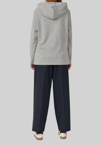 Grijze hoodie, zachte stof, relaxte pasvorm, met een capuchon. Gecombineerd met marineblauwe wijde broek, met een textuurpatroon, en bruine accenten op de schoenen.